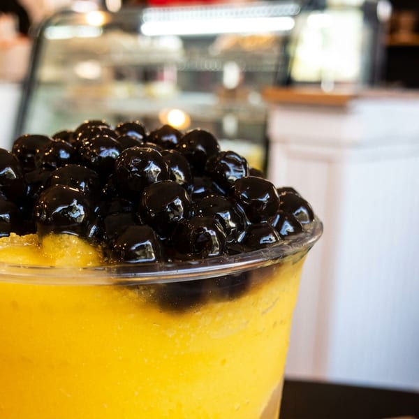 Close-up of a mango boba tea with dark tapioca pearls in a plastic cup.