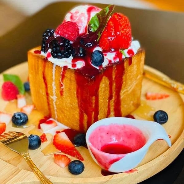 Thick toast topped with ice cream, mixed berries, and berry syrup on a wooden plate.