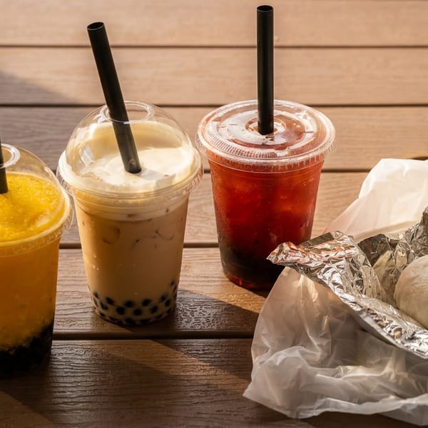Three bubble teas and a steamed bun in foil on a wooden table.