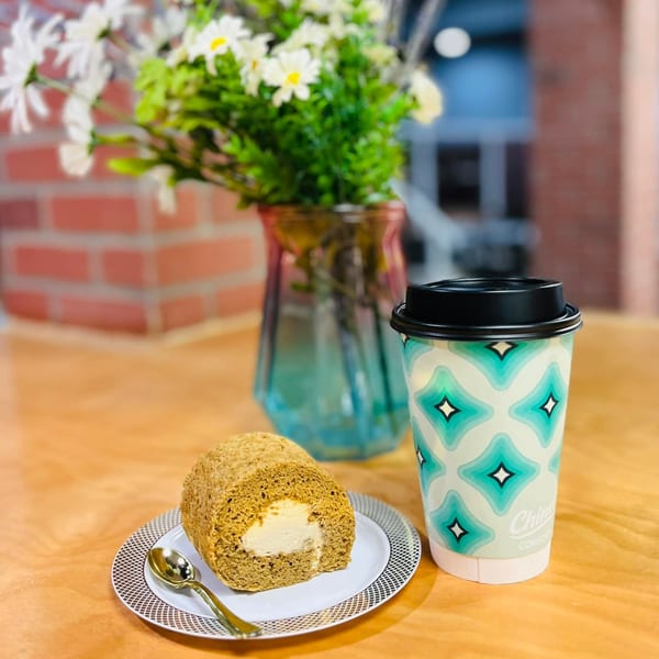 A slice of cake roll with cream filling on a plate next to a patterned coffee cup.
