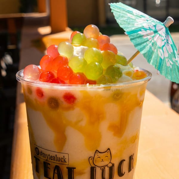 A colorful bubble tea with red and green popping boba, whipped cream, and a small umbrella.