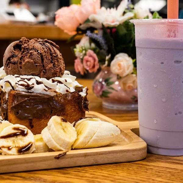 Chocolate toast with ice cream, whipped cream, banana slices, and a purple drink on a wooden table.