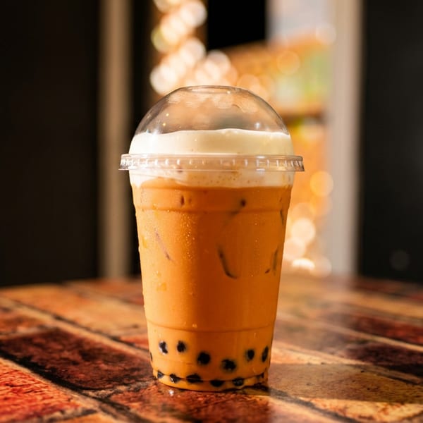 Iced Thai tea with boba and cream topping in a plastic cup on a brick table.