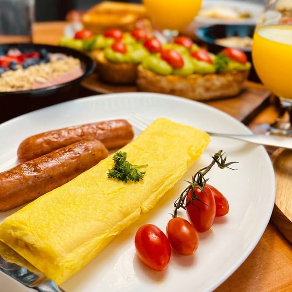 Breakfast spread with an omelet, sausages, cherry tomatoes, avocado toast, and a smoothie bowl.