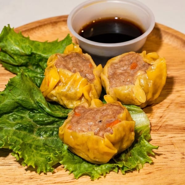 Three steamed dumplings with meat filling and lettuce on a wooden plate with soy sauce.